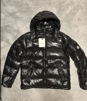 Moncler Maya jacka storlek 4 - Säljer en helt ny och oanvänd Moncler Maya dunjacka i svart, storlek 4 (L/XL). Jackan levereras med samtliga etiketter, tags och Monclers autenticitetsbricka. Både QR-kod, RFID-tagg och NFC fungerar och länkar dig direkt via Monclers officiella hemsida. Perfekt som julklapp eller till dig som vill ha en varm, lyxig och tidlös vinterjacka från ett av världens mest exklusiva märken. #Moncler #MonclerMaya #Dunjacka #Lyxmärke #Designerjacka #Vinterjacka #Fashion #Streetwear #E