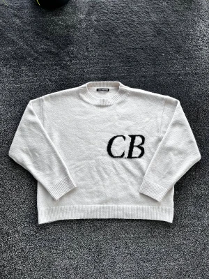 Cole Buxton stickad tröja - Vit stickad tröja från Cole Buxton med svart CB-logo på bröstet. Tröjan har rund hals, ribbade muddar och en loose passform. Materialet är mjukt och grovstickat, perfekt för dig som gillar enkel men stilren design. Storlek M, skick 8/10 har en fläck men borde gå bort i tvätten. Pris går att diskutera✅