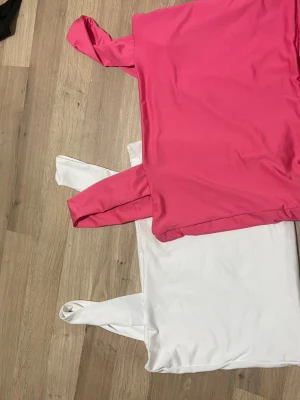 Rosa och vit linnetopp i polyester - Två stilrena linnetoppar i storlek M, en i stark rosa och en i klassiskt vitt. Båda har breda axelband och är tillverkade i mjuk, stretchig polyesterblandning. Perfekta att matcha med jeans eller kjol för en fräsch look.