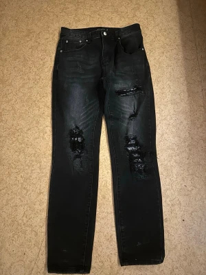 Svarta skinny jeans från Hesntls - Svarta jeans från Hesntls i skinny fit med slitna detaljer och trasiga partier på framsidan av benen. Klassisk femficksmodell med knapp och dragkedja. Jeansen har en mörk tvätt och är tillverkade i stretchigt denim för en tajt passform.