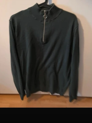 Svart långärmad tröja med half zip - Mörk, grön långärmad tröja med hög krage och snygg half zip-dragkedja framtill. Enkel och stilren design som passar perfekt till jeans eller cargobyxor. Materialet känns mjukt och bekvämt, perfekt för kyligare dagar.