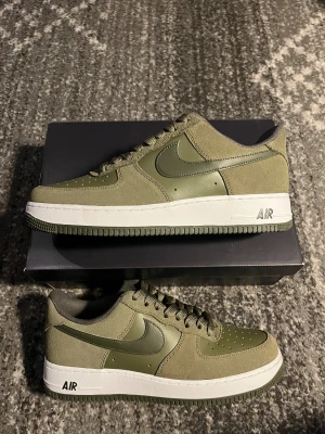 Nike Air Force 1  - Nike Air Force 1 sneakers i olivgrönt med både mocka och skinnpaneler. Snygg låg modell med klassisk vit sula och gröna detaljer, inklusive snörning och yttersula. Ikonisk Swoosh på sidan och perforerad tå för extra stilpoäng. Pris är förhandlingsbart 