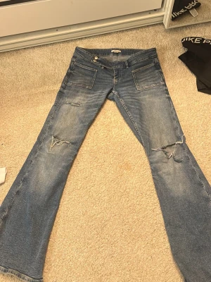 Blå bootcut jeans med slitningar - Säljer ett par blå bootcut jeans från Gina 14+ med snygga slitningar på knäna och framsidan.  Strl L