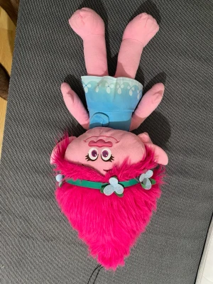 Blå väst till Trolls Poppy mjukisdocka - Säljer en blå väst till Trolls Poppy mjukisdocka. Västen är ljusblå med vita droppformade detaljer längs kanten och har en enkel, rak form. Passar perfekt till Poppy-dockan och ger en färgglad och lekfull look.