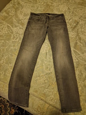 Grå slim jeans från Jack & Jones - Snygga grå jeans från Jack & Jones med slim passform och klassisk femficksdesign. Modellen Glenn sitter tajt men är ändå bekväm, perfekt för dig som gillar en modern look. Jeansen har diskret tvättad effekt och är gjorda i mjukt jeanstyg.