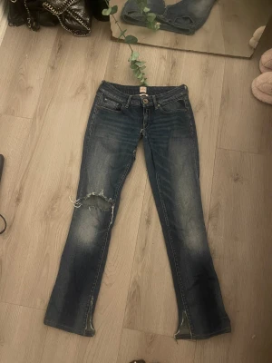 Replay Vicki blå bootcut jeans - Snygga blå jeans från Replay, modell Vicki, med bootcut och slitning på vänster knä för en cool, avslappnad vibe. Klassisk femficksdesign, låg midja och detaljerade bakfickor med gul söm. Jeansen är tillverkade i jeansmaterial med dragkedja och knapp.