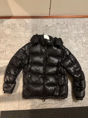 Svart dunjacka Polo Ralph Lauren M - Säljer en svart pufferjacka från Polo Ralph Lauren i storlek M. Jackan har glansig finish, huva, två dragkedjefickor och hel dragkedja framtill. Perfekt för kalla dagar och riktigt skön att bära. Klassisk och stilren design. ÄKTA RALPH LAUREN JACKA