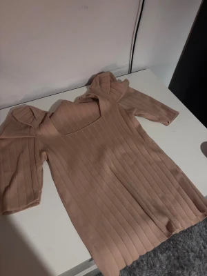 Beige ribbad topp med puffärm - Säljer en beige ribbad topp med fyrkantig halsringning och snygga puffärmar. Toppen har en slim passform och är tillverkad i ett mjukt, stretchigt material som sitter skönt mot kroppen. Perfekt för dig som gillar stilrena detaljer och vill ha något som sticker ut lite extra.