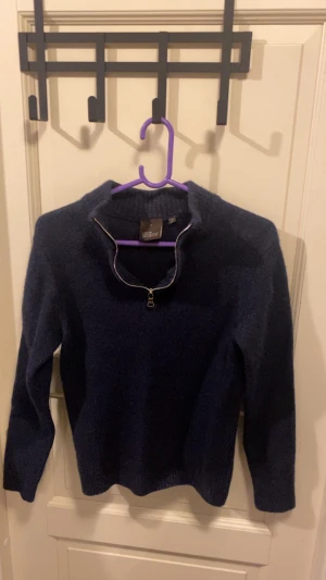 Marinblå stickad tröja Oscar Jacobson - Snygg marinblå stickad tröja från Oscar Jacobson, tillverkad i Italien. Tröjan har en half zip-dragkedja vid halsen och är långärmad med ribbade muddar. Perfekt för dig som gillar klassisk stil med en modern touch.