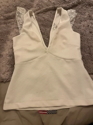 Vit v-ringad topp från Miss Selfridge - Säljer en vit ribbad topp från Miss Selfridge i storlek 36. Toppen har djup v-ringning med spetsdetaljer. Materialet är mjukt och stretchigt, vilket gör den bekväm och snygg. Tveka inte på att skriva till mig vid några frågor, tvättar allt innan jag skickar det💗