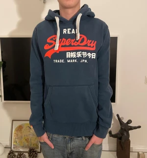Superdry hoodie  - Snygg superdry hoodie i storlek M. Modellen är 187cm. Obs, har 2 små fläckar på ryggen. Borde gå bort i tvätten. Hör av dig vid minsta fundering🤗