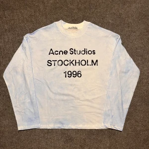 Ljusblå långärmad Acne Studios t-shirt - Snygg ljusblå långärmad t-shirt från Acne Studios med tryck 'STOCKHOLM 1996' i svart på framsidan. Rund hals och relaxed passform. Perfekt för dig som gillar stilrena och trendiga plagg med statement-tryck.