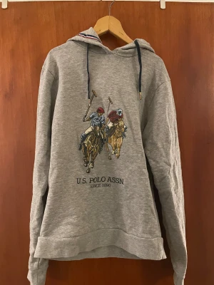 Hoodie från U.S. POLO ASSN. - En gråmelerad hoodie med trycket U.S POLO ASSN. Since 1890. Knappt använd. Storlek S. 90%bomull 10%viskos. Ganska tight passform. 