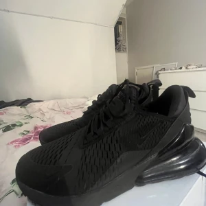 Nike Air Max 270 helsvarta sneakers - Säljer ett par helsvarta Nike Air Max 270 sneakers med snygg mesh-överdel, tydlig Air Max-bubbla i hälen och diskreta swoosh-detaljer. Skorna har snörning och en sportig vibe, perfekta för dig som gillar streetwear och vill ha något stilrent och bekvämt.