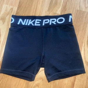 Svarta träningsshorts från Nike Pro - Säljer ett par jättefina svarta Nike Pro träningsshorts.  De passar till träning men också bara vardagligt och under kjolar. Nike loggan har slitits bort men annars är de så gott som nya. De har en elastisk midja med logotyp och är perfekta för intensiva träningspass. Shortsen är tillverkade i ett syntetmaterial som andas och håller dig sval. Nypris ca 350 kr💕