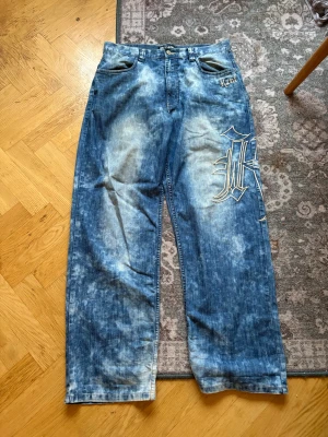 Kani wide jeans med broderi - Säljer ett par blå, blekta jeans från Karl Kani med bred passform och stora broderade Kani-loggor på både fram- och baksida. 