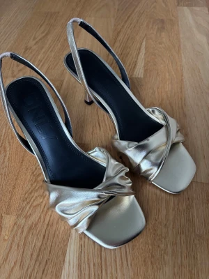 Guldiga klackar från ONLY jul nyår - Snygga klackar i guld från ONLY med låg klack och fyrkantig tå. Skorna har en elegant tvistad rem framtill och smala slingback-band. Aldrig använda, bra skick. Perfekta till jul/nyår!