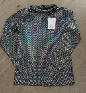 Glittrig långärmad polotopp från Rodebjer helt ny - En supersnygg topp som kan stylas upp eller ner. Den har en hög halsringning, långa ärmar och en slimmad passform.  Helt ny