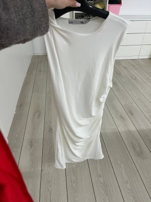 Vit långklänning med drapering - Säljer en vit långklänning från 15th med snygg drapering på sidan. Klänningen har rund halsringning och är ärmlös, vilket ger en clean och modern look. Perfekt för dig som gillar minimalistisk stil och vill sticka ut med enkla detaljer.