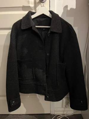 Kappa - Snygg mörkgrå jacka från Lager 157 i ullblandning. Klassisk krage, stora framfickor och knäppning med stora knappar framtill. Perfekt för dig som gillar en stilren och enkel look. Jackan har lång ärm och rak passform.