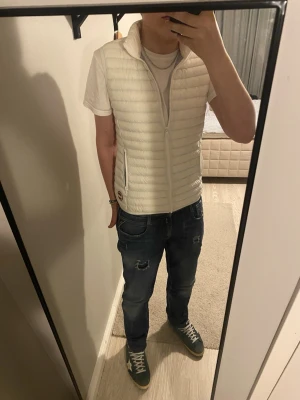 Vit dunväst från Colmar - Snygg vit dunväst från Colmar med quiltad design och hög krage. Västen har två praktiska fickor med dragkedja och ett tydligt Colmar-märke på framsidan. Perfekt att slänga över en hoodie eller t-shirt för en clean look. Storlek S sitter tajt och fint runt kroppen, ny pris 1600kr