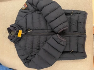 Mörkblå  pufferjacka från Parajumpers - Säljer en mörkblå pufferjacka från Parajumpers i barn storlek med coolt patch på ärmen och gul detalj vid kragen. Jackan är superlätt, har dragkedja framtill och två sidofickor med zip. Perfekt för kalla dagar och har en snygg, sportig look.