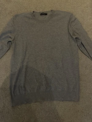 Grå stickad tröja från J.Lindeberg - Snygg grå stickad tröja från J.Lindeberg i klassisk modell med rund hals och långa ärmar. Storlek M