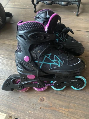 Inlines strl 31-34 - Coola inlines med svart, lila och turkosa detaljer, designad med sportig känsla och grafiskt mönster. Inlinesen har en modern form och är tillverkad i syntetmaterial med justerbara spännen och meshpartier för extra komfort. Perfekt för dig som gillar att sticka ut med färg och stil.