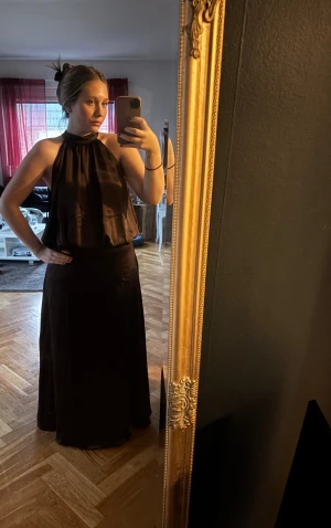 Brun satin halterneck maxiklänning  - Säljer denna otroliga bruna maxiklänningen! Den är i satin och passar perfekt till bal eller bara som en elegant långklänning. Den är endast testat hemma och har också lappen kvar. Den börjar ta slut i de flesta butiker!