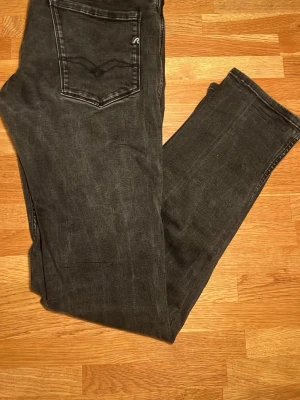 Replay Anbass svarta jeans - Svarta Replay Anbass jeans med klassisk femficksdesign och diskret logga på bakfickan. Superbra skick utan några defekter. Jeansen har en rak passform och är tillverkade i slitstarkt denimtyg med snygga detaljer vid fickorna. Perfekt för dig som gillar stilrena och tidlösa jeans. Storlekslappen är ej kvar men storleken är 30/32. Pris kan diskuteras! 