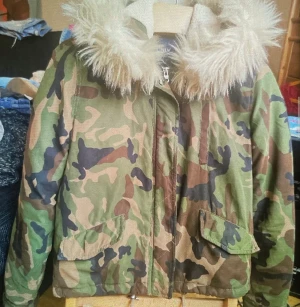 Camouflage jacka med fuskpäls - Säljer en grön camouflage jacka från ONLY med fluffig fuskpäls på huvan. Jackan har dragkedja framtill, två fickor med lock och quiltat innerfoder. Perfekt för dig som vill sticka ut med en cool streetstyle-look.