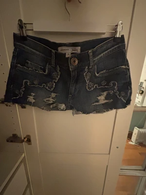 Broderade jeansshorts  - Snygga mörkblå jeansshorts med rå, fransig kant och slitningar. Shortsen har broderade detaljer i vitt på både fram och bak shortsen passar perfekt till nästa sommar