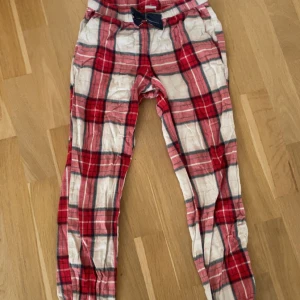 Röd-rutiga pyjamas byxor från Kappahl - Säljer ett par sköna pyjamas byxor från Kappahl i storlek 146/152. Byxorna har ett rött och vitt rutigt mönster, resår i midjan med en blå rosett och är gjorda i mjukt bomullsmaterial. Perfekta för chill hemma eller mysiga dagar.