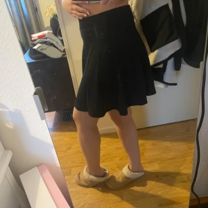 Svart kortkjol i stretchigt tyg - Enkel och snygg svart kortkjol med lätt utsvängd form. Kjolen har en bred resår i midjan och är gjord i ett stretchigt material som sitter bekvämt. Perfekt att matcha med crop tops eller hoodies för en chill look.