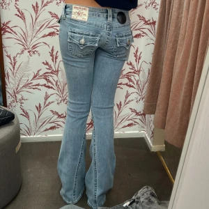 Lågmidjade bootcut jeans True religion - Superpopulära ljusblå jeans från True Religion med klassiska kontrastsömmar och ikoniska fickdetaljer bak. Modellen Joey och har bootcut-ben och en så fin låg midja. Storlek W25 men passar xxs/xs/s. Lite slitna längst  ner på baksidan men är inget som man tänker på så de är i bra skick❤️Midjemåttet är 38 cm och innerbenslängen är 82 cm🫶🏻