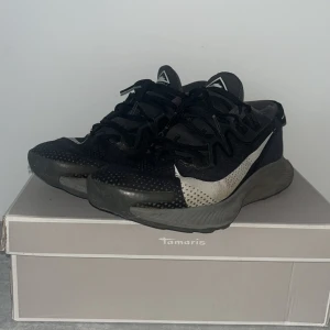 Svarta sneakers från Decathlon - Snygga svarta sneakers från Decathlon med vit logga och detaljer. Skorna har en chunky grå sula och svart snörning. Ovandelen är i mesh-liknande syntetmaterial som andas och ger en sportig vibe. Perfekta för dig som gillar streetstyle och bekväma skor.