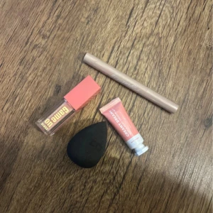 Sminkkit med läppglans och beautyblender - Säljer ett sminkkit med ett genomskinligt läppglans från makeupmekka med korallfärgat lock, en persikofärgad Creamy Dreamy krämrouge, en svart droppformad beautyblender och en beige ögonbrynspenna. Perfekt för en fräsch look. Allt är oanvänt