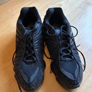 Nike Shox svarta sneakers strl 46 - Nike Shox sneakers i helsvart med cool fjädrande sula och meshdetaljer. Skorna har snörning och en sportig look med diskreta Nike-loggor på sidan. Ovandelen är i syntet och mesh för bra ventilation. Perfekt för dig som gillar streetstyle och sportig vibe. Storlek 46, men upplevs som något små i storleken. 