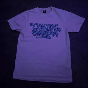 Vit t-shirt FSBN Chaotic System S - Fräsch vit t-shirt från FSBN i storlek S med blått graffiti-tryck 'Chaotic System' på bröstet. Klassisk rund hals och korta ärmar, tillverkad i mjuk bomull. Perfekt för dig som gillar streetstyle och coola prints.