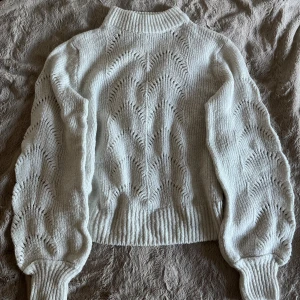 Vit stickad tröja - Superfin vit stickad tröja med unikt vågigt hålmönster. Tröjan har långärmade ballongärmar och en ribbad hög krage som ger en snygg och trendig look. Perfekt för hösten och vintern.