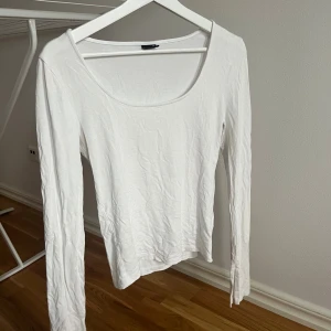Vit långärmad topp med slits i ärmen - En enkel och fräsch vit långärmad topp med rundad halsringning. Modellen är rak och har en clean look som funkar till allt. Materialet känns mjukt och lätt, perfekt för layering eller att bära som den är. Snygg att styla med jeans eller kjol.