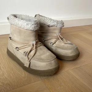 Beige moon boots från Everest strl 37 - Moon boots från Everest i beige med fluffigt foder och snörning runt om. Yttermaterialet är syntet och mocka, med en platt sula som har mönstrad undersida för extra grepp. 1 år gamla vuxit ur
