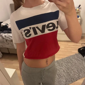 Levi's croppad t-shirt i rött, blått och vitt - Säljer en croppad t-shirt från Levi's med klassisk logga. T-shirten har breda block i rött, blått och vitt, korta ärmar och rund hals. Storleken har tvättats bort så kan inte se vilken storlek men skulle säga xs/s