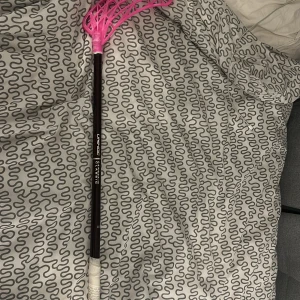 Unihoc carbskin Classic Floorball Stick - Unihoc Classic innebandyklubba med svart skaft och rosa blad. Grepptejpen är vit och visar tecken på användning, men klubban är i gott skick utan synliga sprickor. Perfekt för både träning och match. Lätt och hållbar design för optimal spelupplevelse.