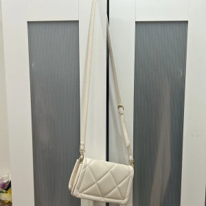 Vit axelväska med lång rem - Väska köpt i primark som jag har använt ett flertal gånger i början men inte nu längre. Den har blivit lite smutsig inuti som man ser i bilderna men inget som märks på utsidan av väskan. Jättefin väska som passar till alla outfits:)