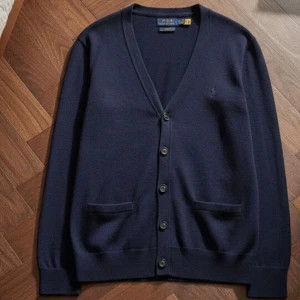 Marinblå kofta från Polo Ralph Lauren - Klassisk marinblå kofta från Polo Ralph Lauren med v-ringning, knappar framtill och två fickor. Diskret broderad logga på bröstet. Perfekt för lager-på-lager och enkel att matcha med allt. Skön och stilren design.