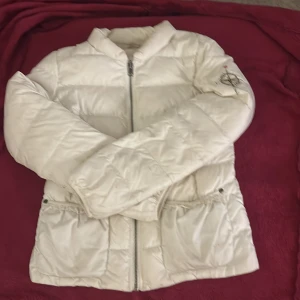 Vit pufferjacka från Odd Molly - Säljer en vit pufferjacka från Odd Molly med snygga detaljer som en broderad kompass med hjärta och blommor på ärmen samt en stor svartvit fjäril på ryggen. Jackan har dragkedja framtill och två fickor med knappstängning. Perfekt för dig som gillar unika prints.