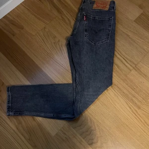 Levi's 512 gråsvarta jeans - Säljer ett par gråsvarta Levi's 512 jeans med klassisk femficksdesign och röd Levi's-tag på bakfickan. Jeansen har en smal passform passar dig som är mellan 170-180cm, och är tillverkade i mjukt denimtyg. Perfekta för dig som gillar en stilren och tidlös look. Skriv vid frågor!