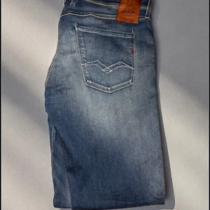 Replay Hyperflex jeans blå W34 L34 - Säljer ett par Replay Hyperflex jeans i klassisk blå tvätt med snygga slitningar. Jeansen har raka ben, femficksmodell och skön stretch. Märkespatch bak i midjan och diskreta detaljer på bakfickorna. Perfekta för dig som gillar stilrena och bekväma jeans.