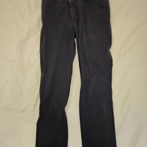 Svarta kostymbyxor Lawrence Grey - Snygga svarta kostymbyxor från Lawrence Grey i klassisk rak modell. Byxorna har sidfickor fram och knäppning med knappar bak. Perfekt för dig som gillar stilrena och tidlösa plagg. Materialet känns mjukt och har en elegant finish. Passar en 30w30L 